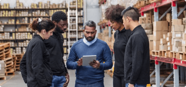 Team of people interact with a tablet while standing in a warehouse